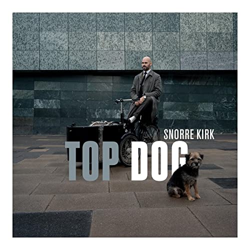 A man in a suit sits on a cargo bike with a dog nearby.