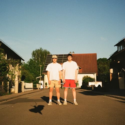 Two young men standing on a street in front of houses.