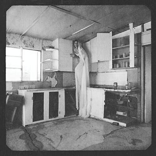 Black and white photo of a person in a white dress in a kitchen.