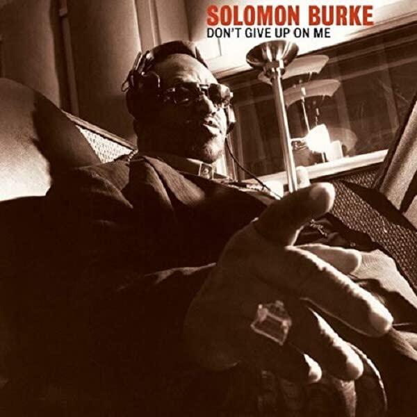 Solomon Burke wearing headphones and sunglasses, pointing toward the camera in a sepia-toned studio.