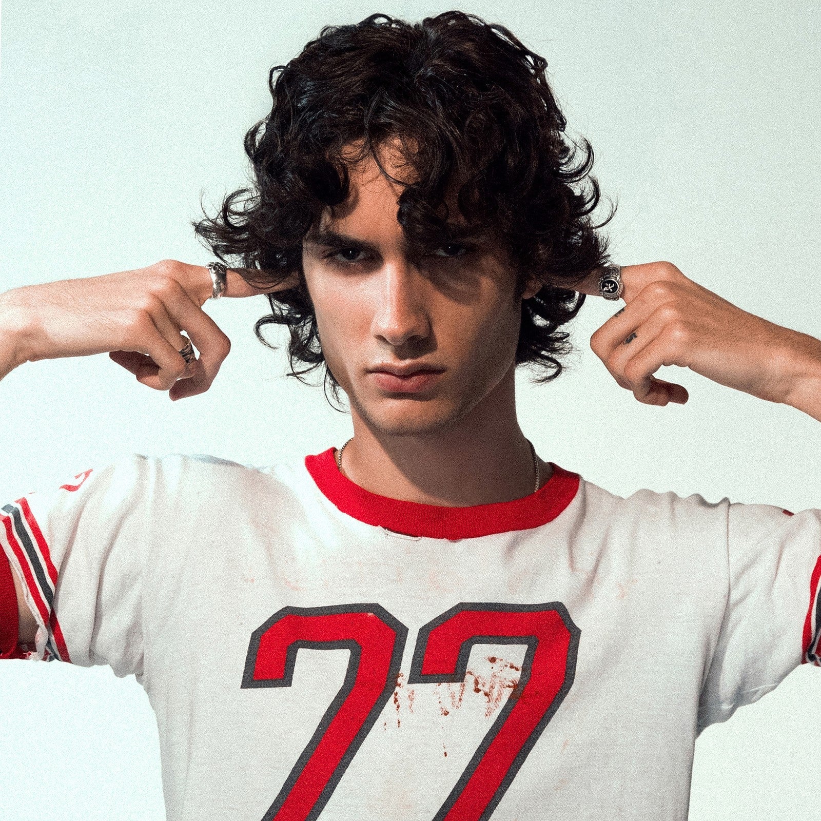 Sombr portrait: young man with curly hair, wearing a white jersey.