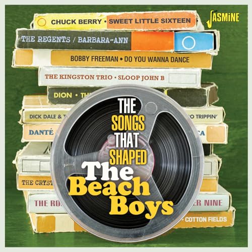 A reel-to-reel tape sits in front of a stack of vintage music cassette cases.