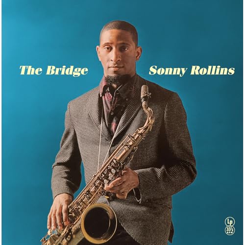 Sonny Rollins in a suit holding a saxophone against a solid blue background.
