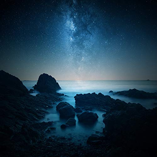 Rocky coastline under a vibrant, starry night sky.