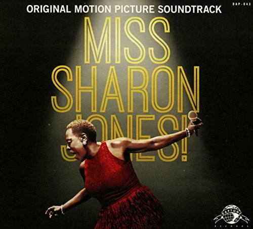Sharon Jones singing in a red dress under a spotlight on a dark background.