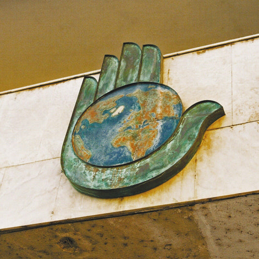 Bronze hand cradling a colorful, textured globe against a tiled wall.