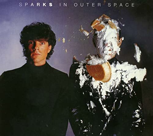 Two men in black, one with a pie smashed on his face and suit.