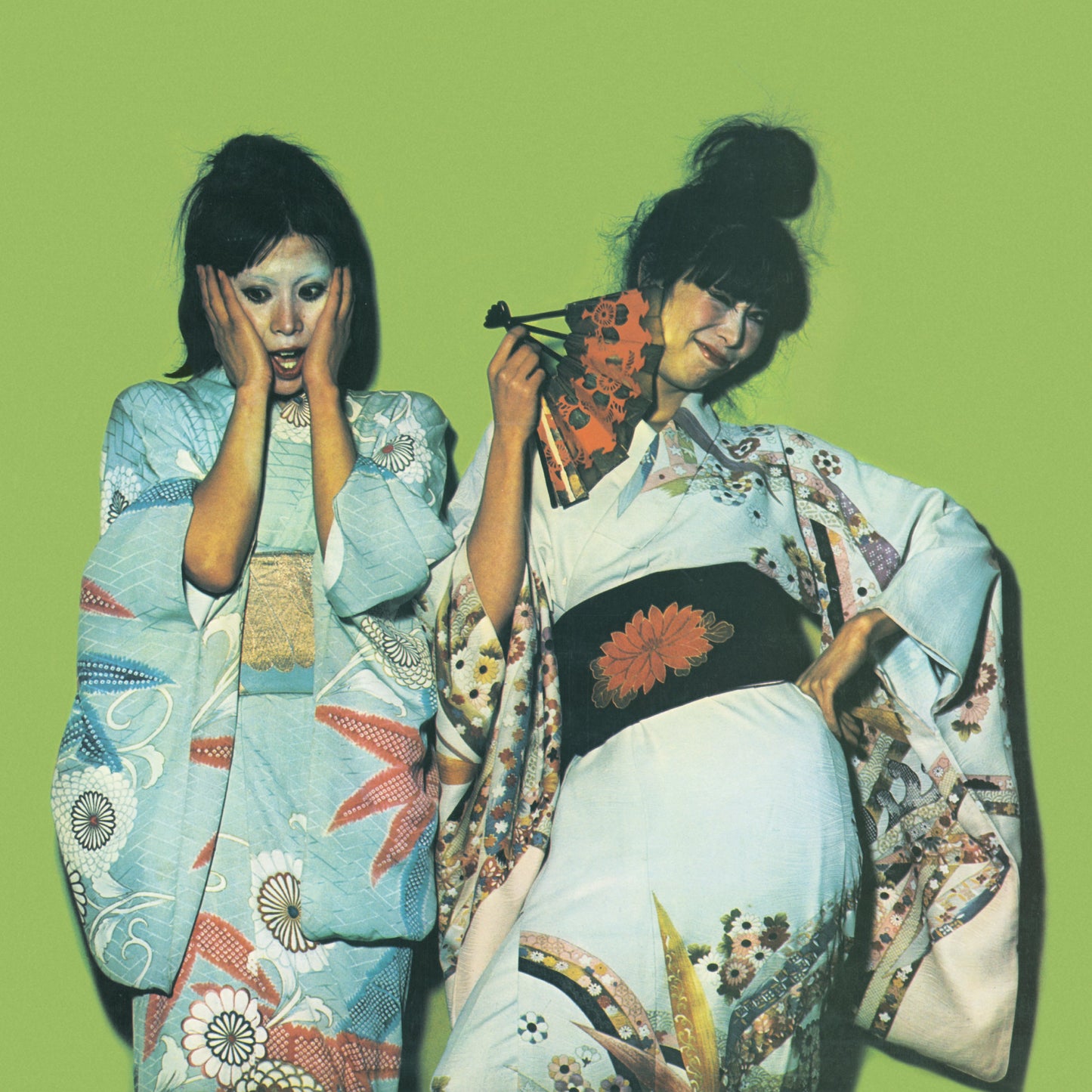 Two people in patterned kimonos pose against a bright green background.