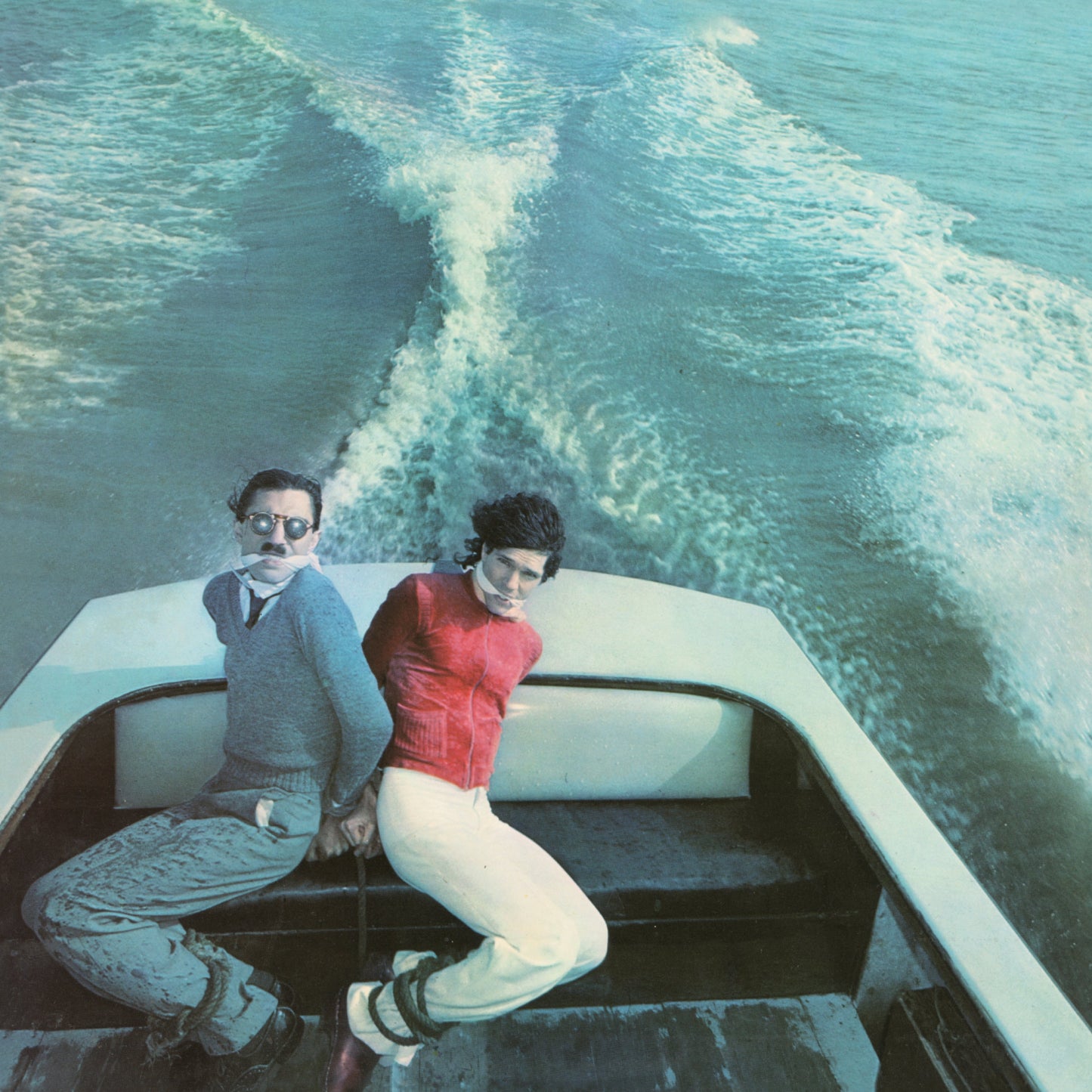 Two men on a speeding boat, viewed from behind, album cover.