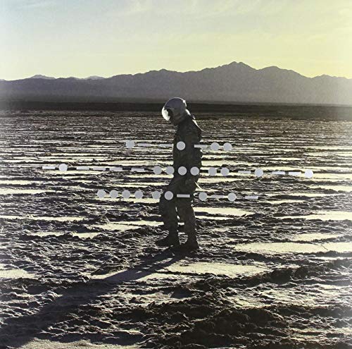 Person in a spacesuit stands in a desert landscape.