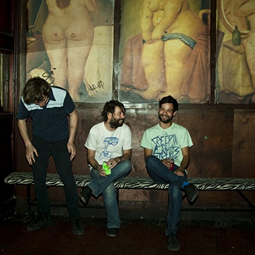 "Three men sitting on a zebra-print bench, with nude paintings on the wall behind."