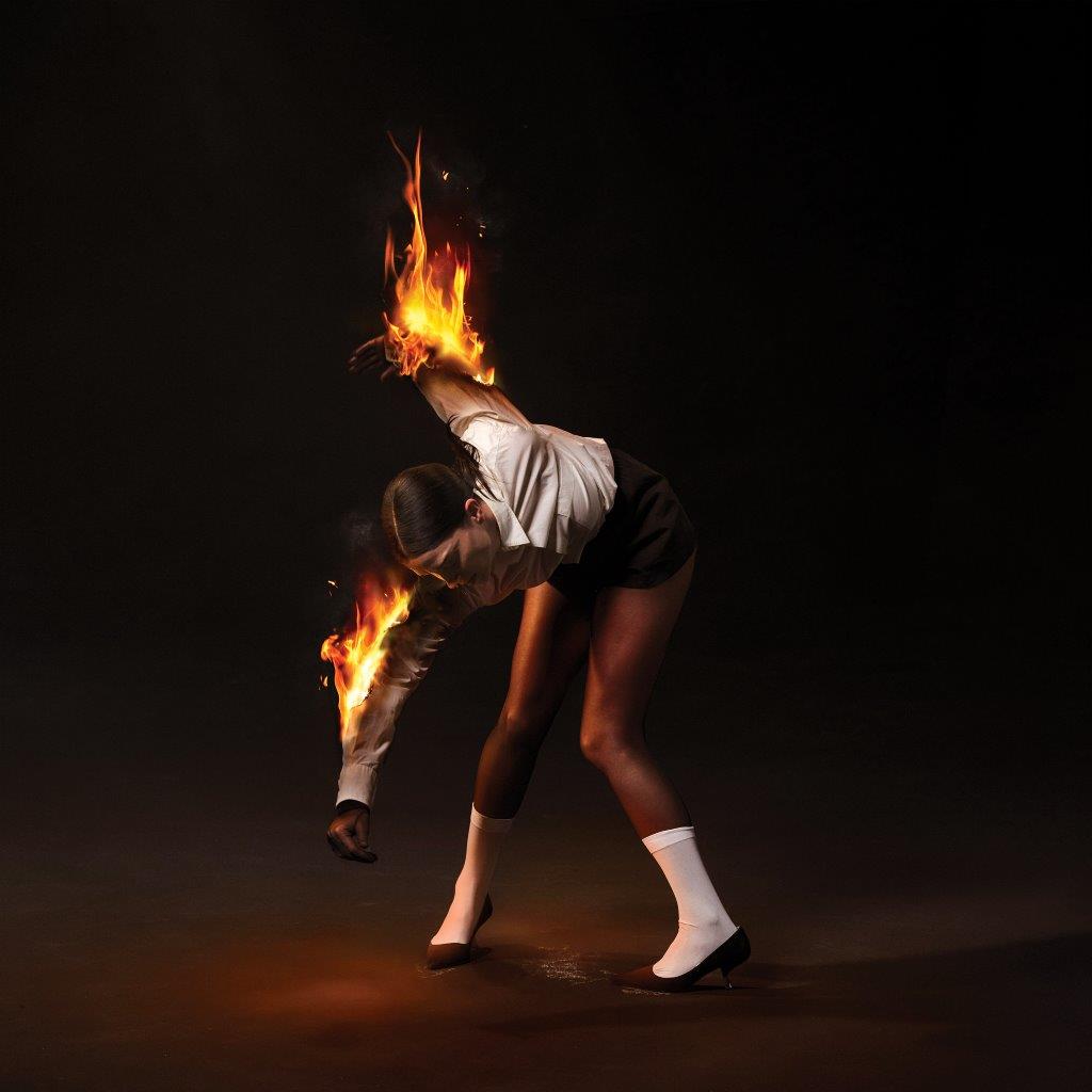 Woman with flames erupting from her arm and clothing, dark background.