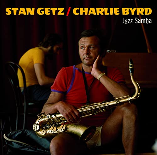 Stan Getz holding a saxophone with Charlie Byrd in the background against dark curtains.