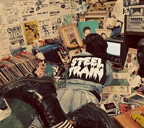 Person wearing a “Steel Train” patch jacket, surrounded by collectibles.