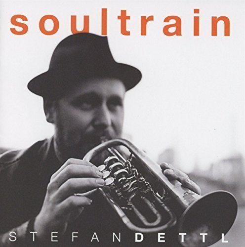 Black and white photo of Stefan Dettl playing a trumpet, with orange text above.