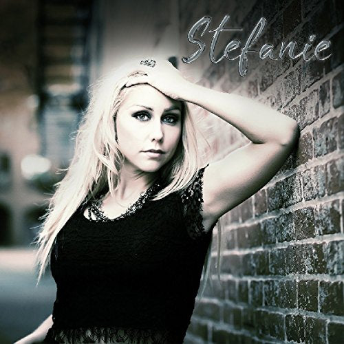Blonde woman with hand to head, leaning against a brick wall.