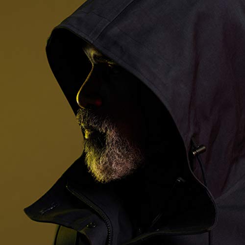 Man wearing a dark hooded jacket, partially lit, against a brown background.