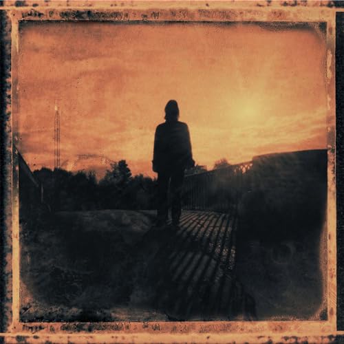 A silhouette of a person standing on a bridge against an orange sunset sky.