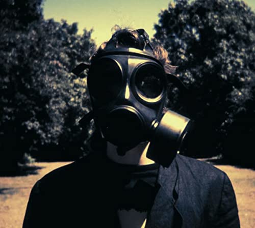 A person wearing a gas mask stands outdoors against a background of dark trees.