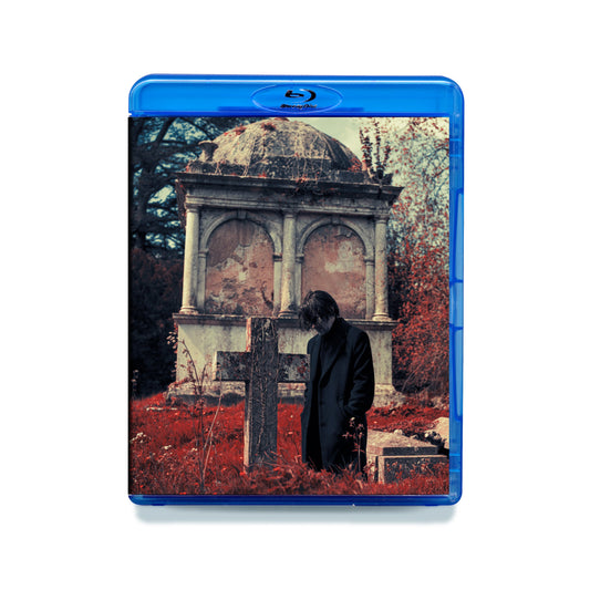 Blu-ray cover: man in coat stands before a stone mausoleum.