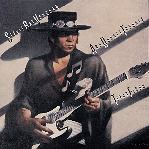 Stevie Ray Vaughan wearing a hat and playing a white electric guitar.