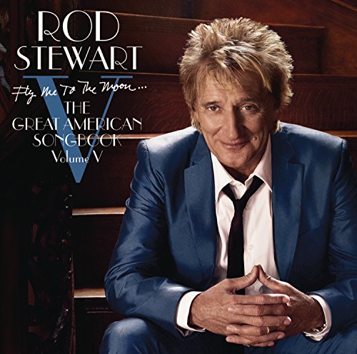Rod Stewart wearing a blue suit and tie, sitting on wooden stairs.