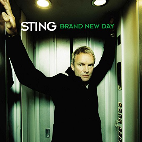 Sting in a dark coat, arms raised in a doorway.