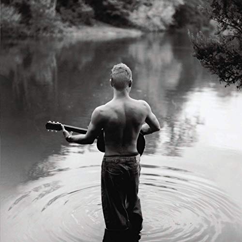 Back view of Sting with a guitar, standing in shallow water.