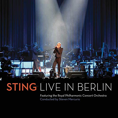 Sting performing with an orchestra on a brightly lit stage.