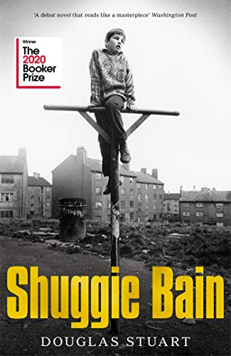 A young boy sits on a metal pole in front of urban housing.