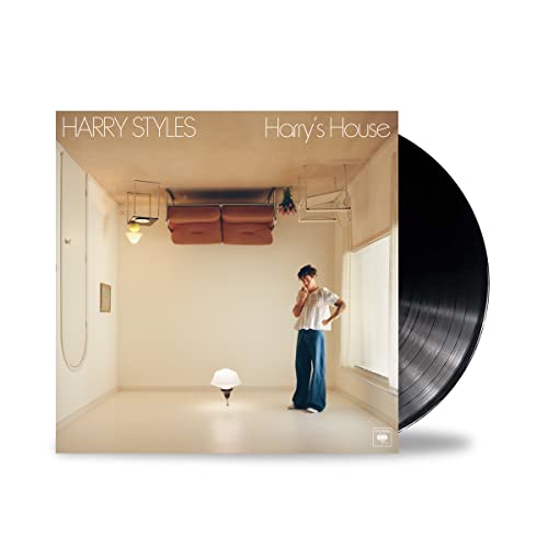 Harry Styles standing in a room with upside-down furniture next to a black vinyl record.