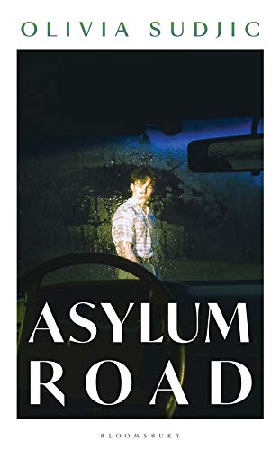 Book cover: "Asylum Road" featuring a man seen through a car windshield.