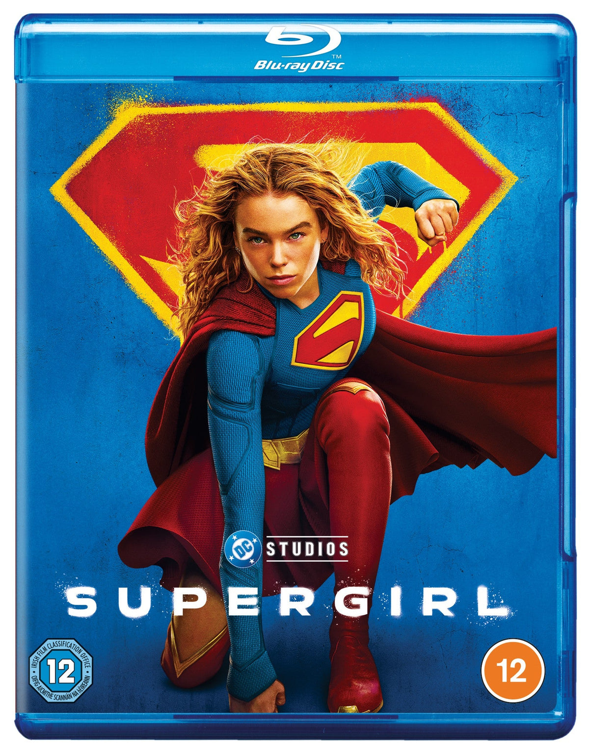 Supergirl stands in a brown coat before a large yellow and red Superman logo.
