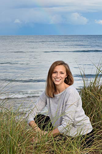 Woman smiling at the camera, sitting in beach grass by the ocean.