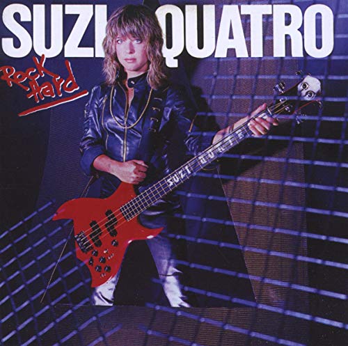 Suzi Quatro playing a red bass guitar on a dark stage.