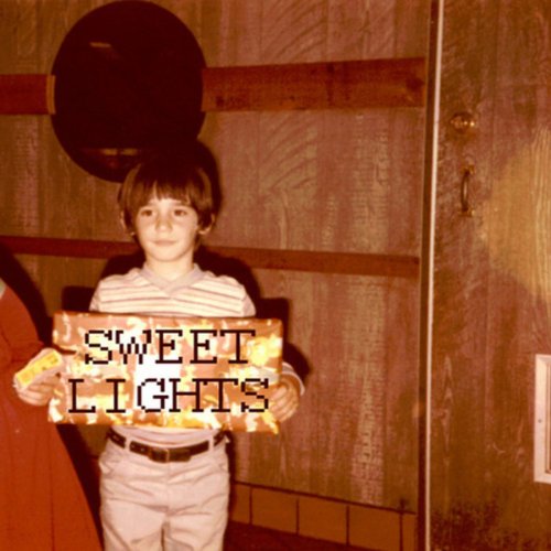 Young boy holding a sign reading "Sweet Lights" indoors.