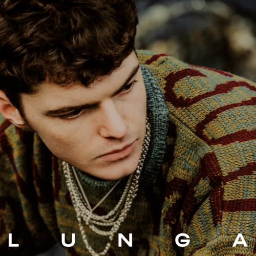 Close-up portrait of a man wearing a patterned sweater and layered silver chain necklaces.