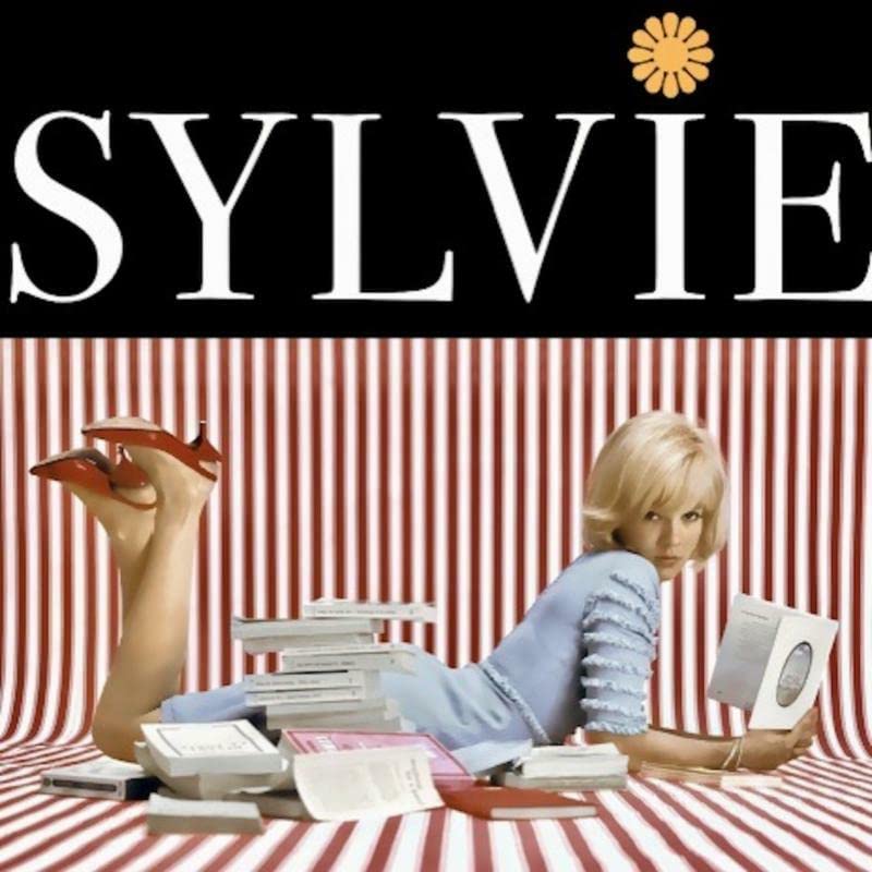 Sylvie Vartan album cover with a woman posing amongst books and records.
