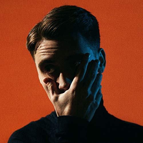 Close-up portrait of a man with hand near his face, orange background.