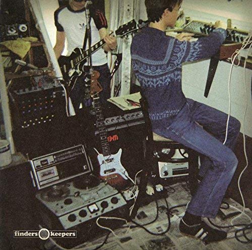 Two musicians playing electric guitar and synthesizer in a cluttered home studio setting.