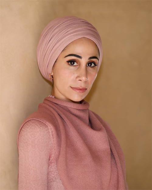 A woman wearing a dusty pink turban and matching knit scarf against a wall.