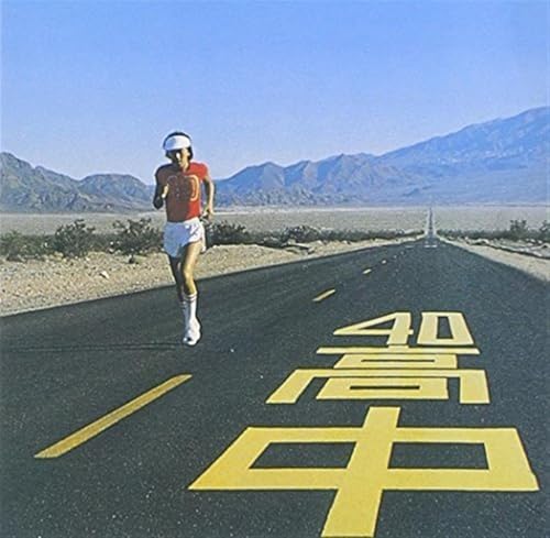Man running on a desert road with large yellow Japanese characters.