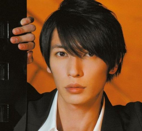 Close-up portrait of Hiroshi Tamaki with dark hair and orange background.
