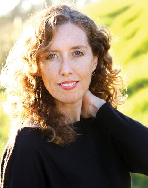 Woman with wavy brown hair and a gentle smile, outdoors.