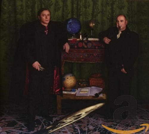 Two men in dark clothing stand before a table with globes.