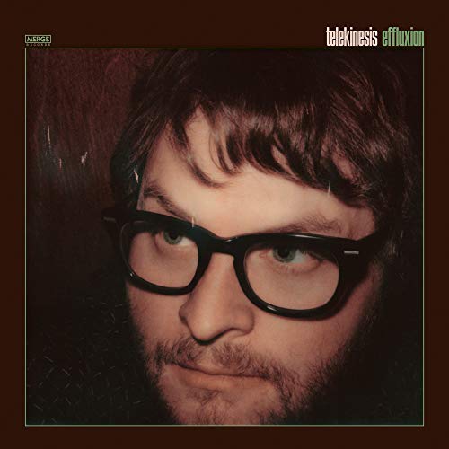 Close-up portrait of a man with brown hair and glasses, album cover art.