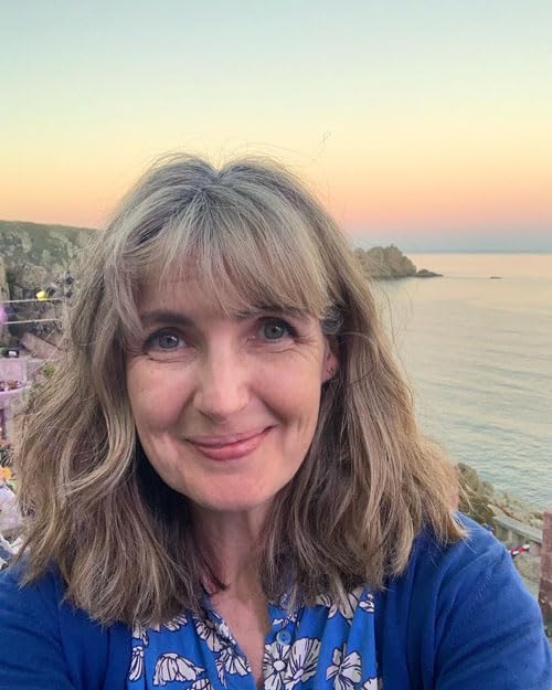 Portrait of a smiling woman with grey-blonde hair against a coastal sunset background.