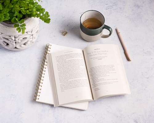 Open book with tea, plant, and pen on a light surface.