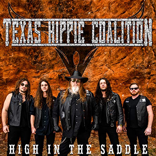 Five band members in leather vests stand before a rocky orange cliff face.