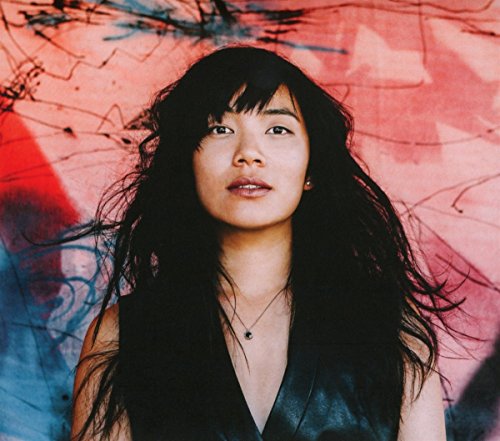 Close-up portrait of Thao, a woman with long dark hair, against a colorful wall.